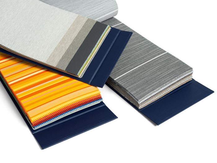 Stapel von Stoffmustern in verschiedenen Farben und Mustern, darunter graue, orange und gestreifte Designs. Stapel von Stoffmustern in verschiedenen Farben und Mustern, darunter graue, orange und gestreifte Designs.