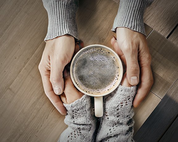 Zwei Hände halten eine Tasse Kaffee gemeinsam auf einem Tisch. Zwei Hände halten eine Tasse Kaffee gemeinsam auf einem Tisch.