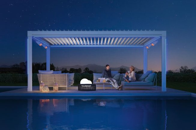 Eine Überdachung mit Sitzbereich über einem Pool bei Nacht, umgeben von sanften Lichtakzenten.