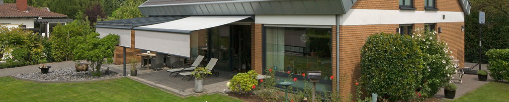 Ein modernes Haus mit einer Überdachung, Markisen und einer Terrassensituation im Garten.