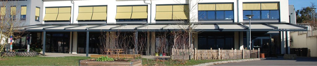 Überdachung vor einem modernen Gebäude mit gelblichen Markisen und großen Fenstern.